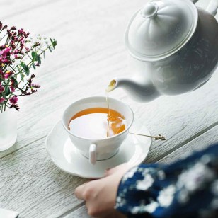 person holding white ceramic teapot and pouring tea in cup